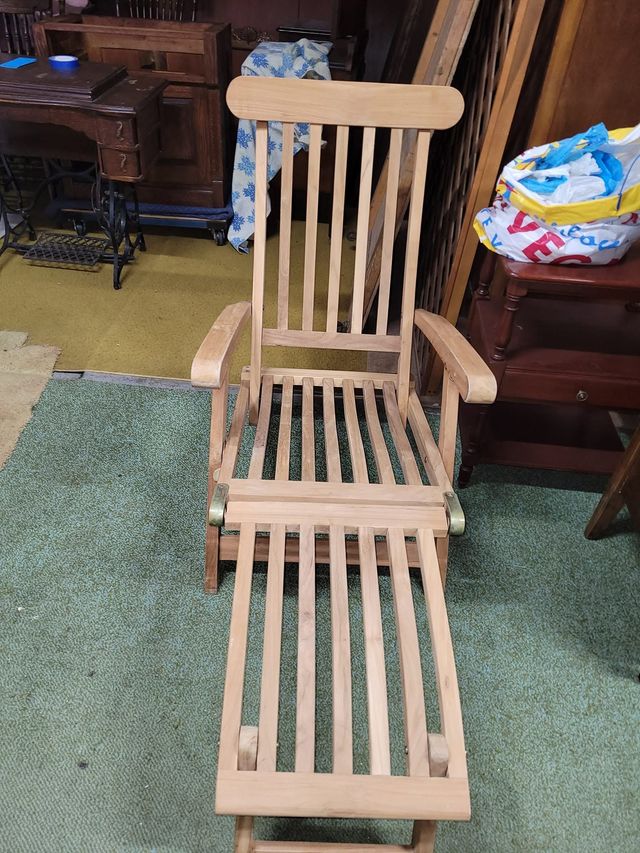Wooden slatted rocking chair with an extended footrest on a carpeted floor.