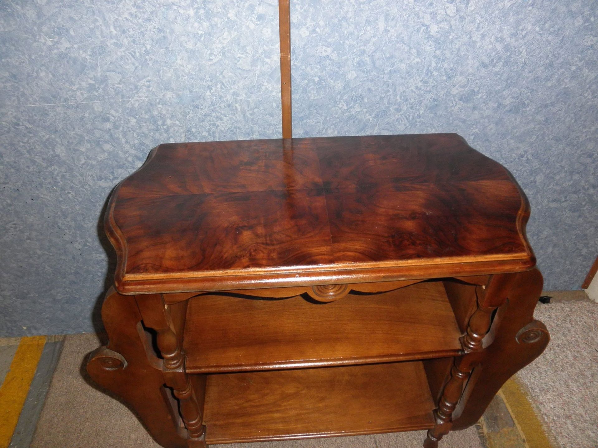 Small wooden side table with curved legs and open shelves against a blue wall.