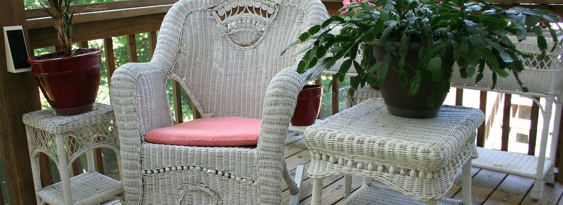 White wicker patio set with pink cushions and potted plants on a wooden deck