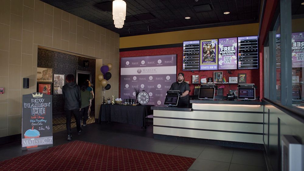 Movie theater lobby with people entering, concession stand, movie posters, and event decor in purple and black.