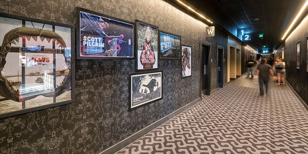 Hallway with artwork and people walking. Black patterned wall and flooring, with gold lighting.
