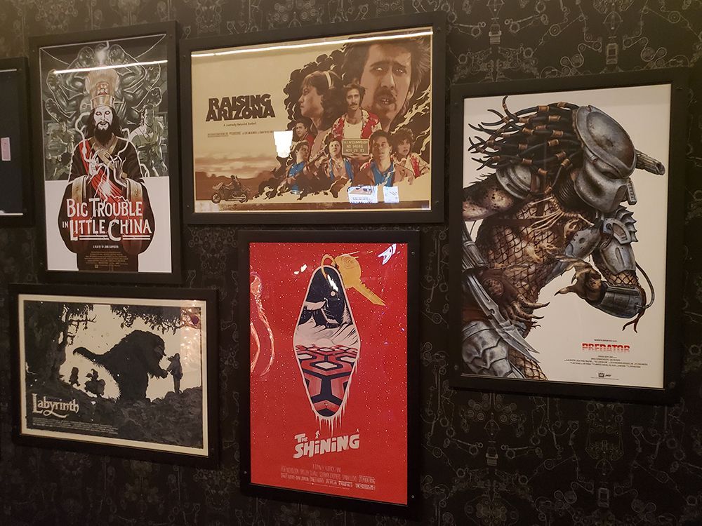 Movie posters framed on a wall: Big Trouble in Little China, Raiders, Predator, The Shining, and Labyrinth.
