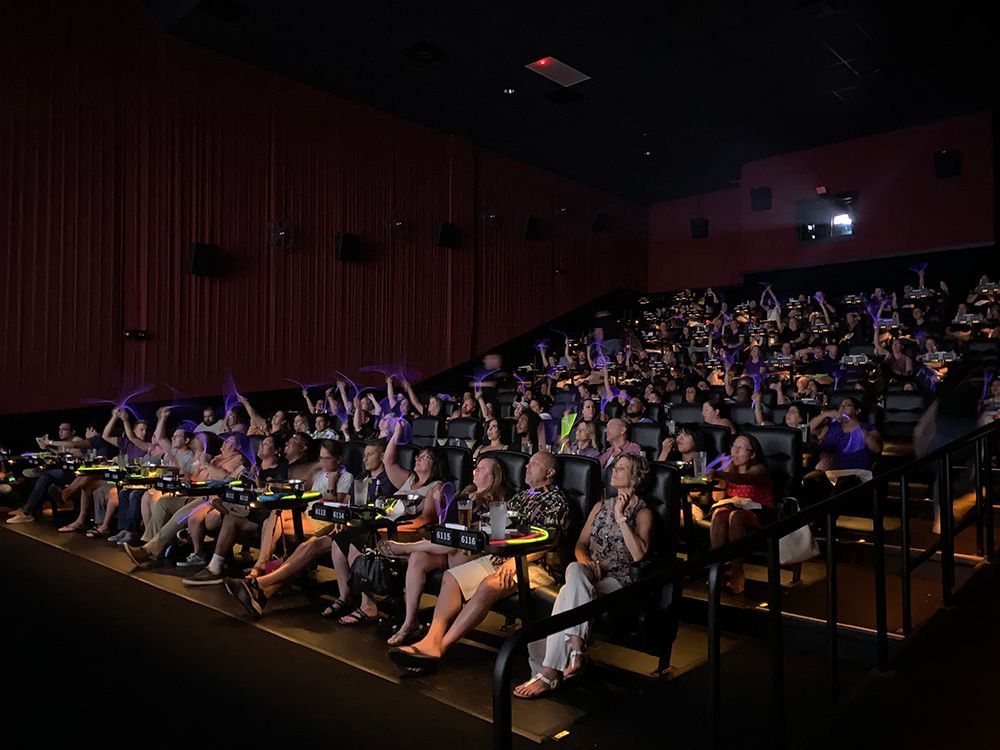Movie theater filled with people waving purple glow sticks.