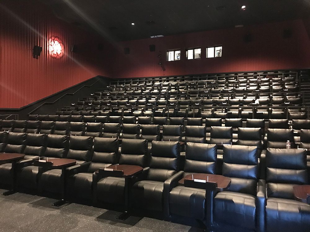 Empty movie theater with black reclining seats and small tables. Red walls and black ceiling.