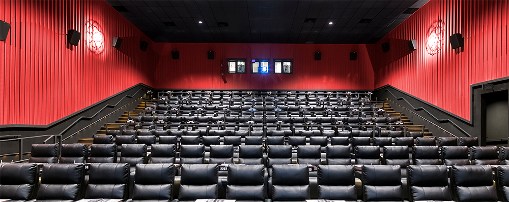 Interior of a movie theater with rows of black seats, red curtains, and a black ceiling.