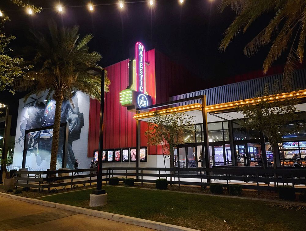 Majestic movie theater at night, lit-up sign, palm trees, colorful exterior, movie posters.