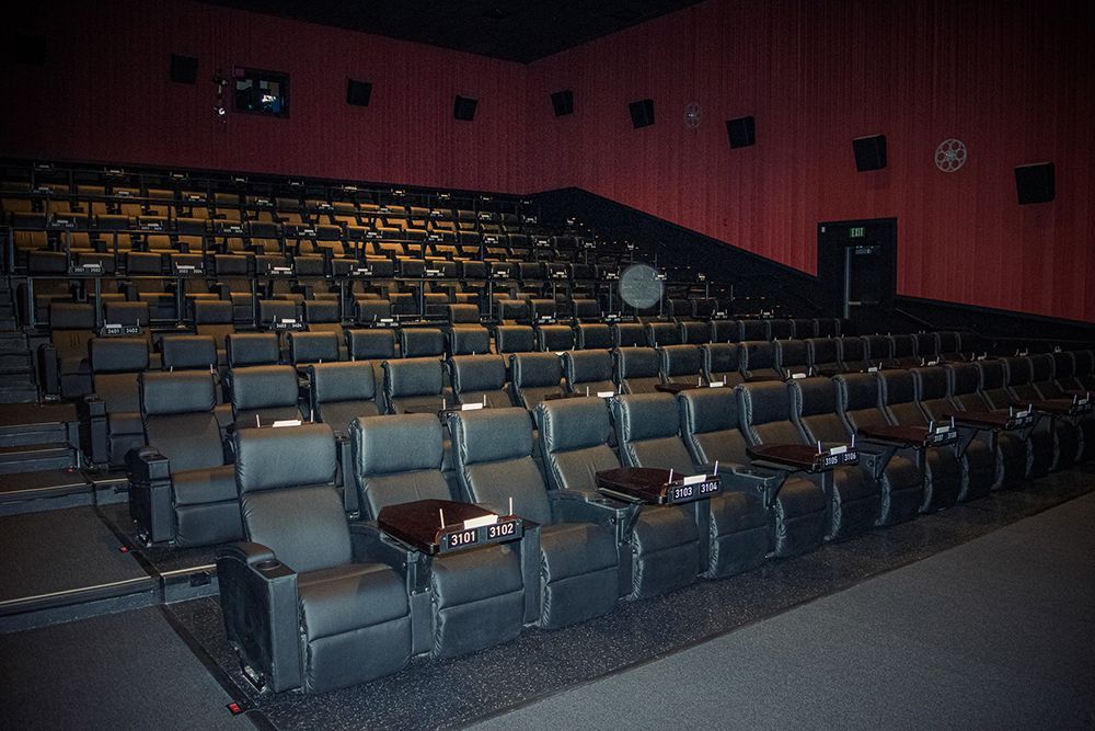 Rows of black, reclining seats in a movie theater with small tables. Red walls, black ceiling.