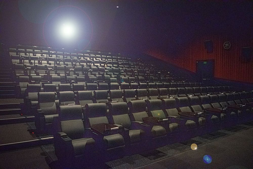 Empty movie theater with rows of black seats, stage with bright light.