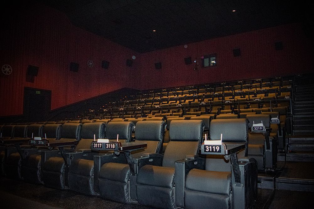 Empty movie theater with rows of black reclining seats. Red walls, black ceiling.