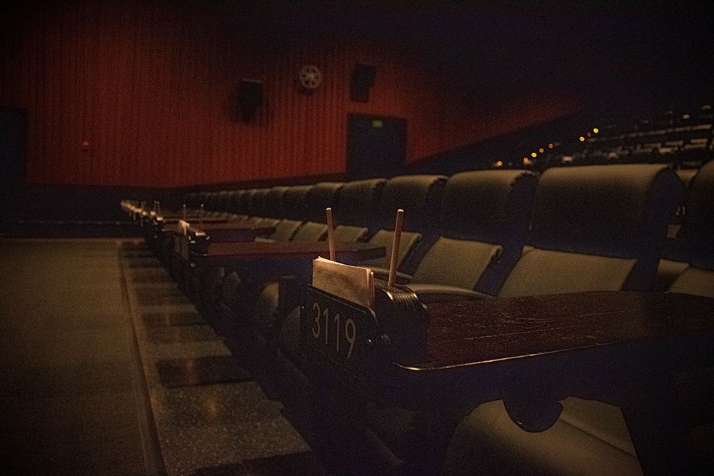 Dark, empty movie theater with rows of black seats and small tables. Red walls and dim lighting.