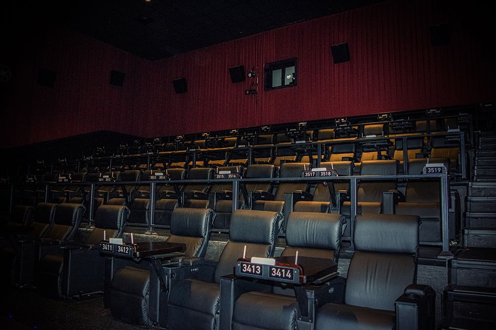 Rows of dark, reclining theater seats in a dimly lit cinema, red wall background.