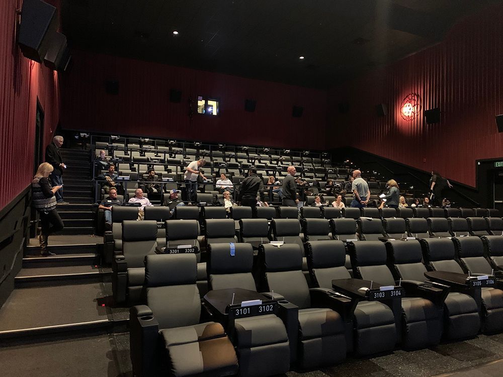 Movie theater interior with rows of black reclining seats. People are seated and walking.
