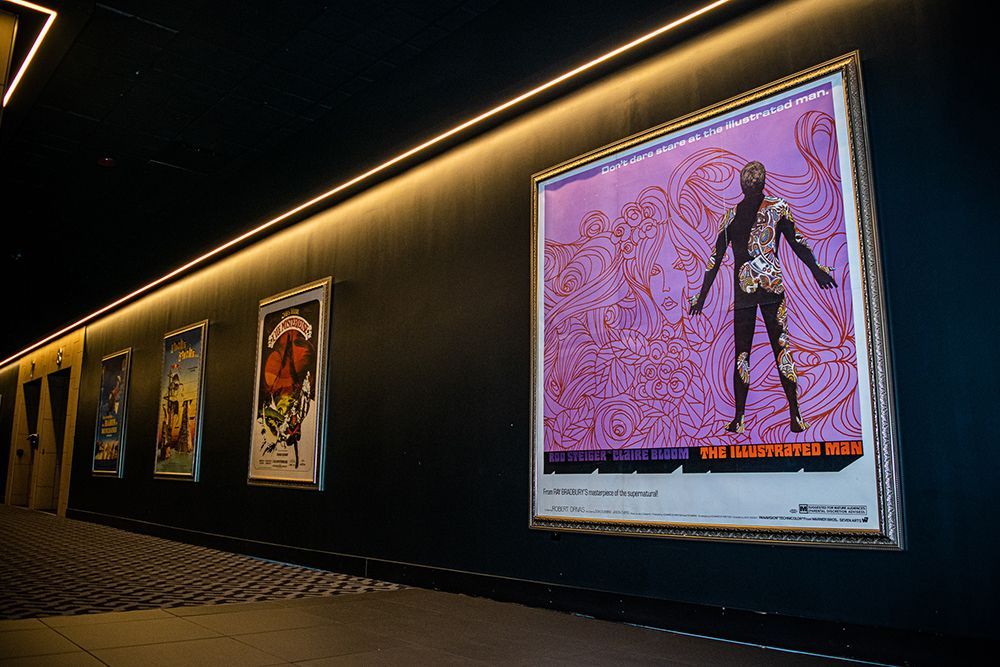 A row of framed movie posters on a dark wall, with a neon light above.