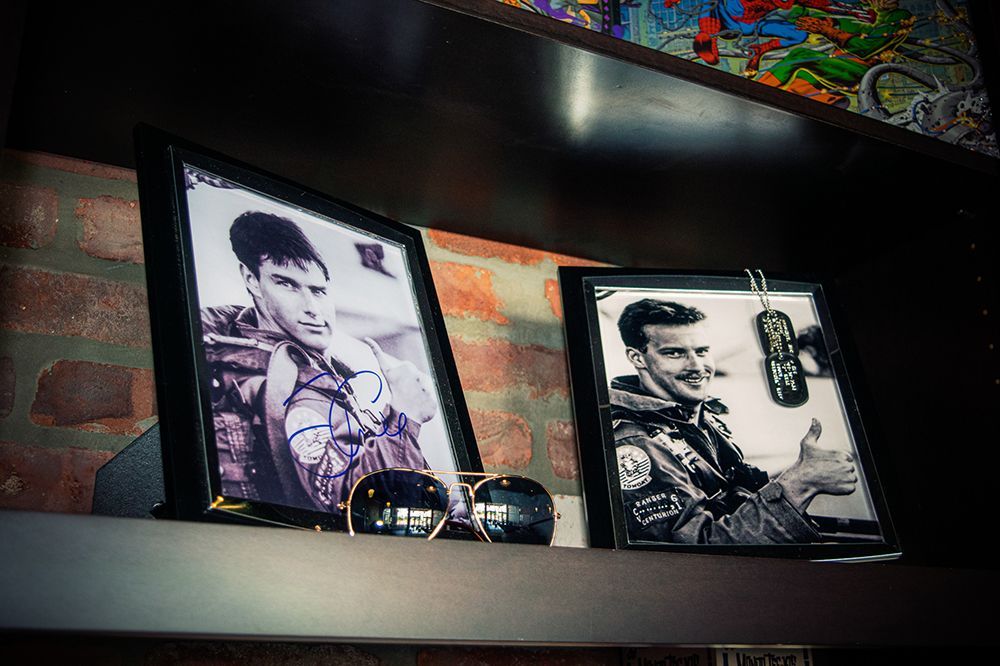 Framed photos of Tom Cruise in Top Gun, sunglasses in front on a shelf.