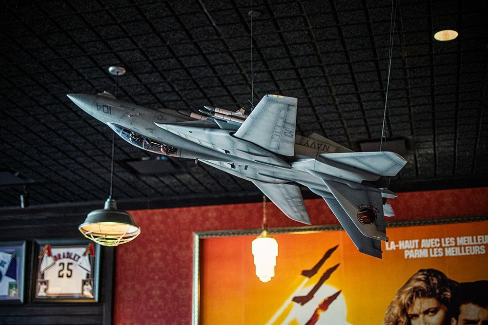 Model airplane suspended from a dark ceiling, near a light fixture and a poster.