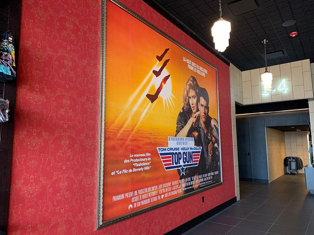 Movie poster for Top Gun inside a theater, with a red wall and a hall.