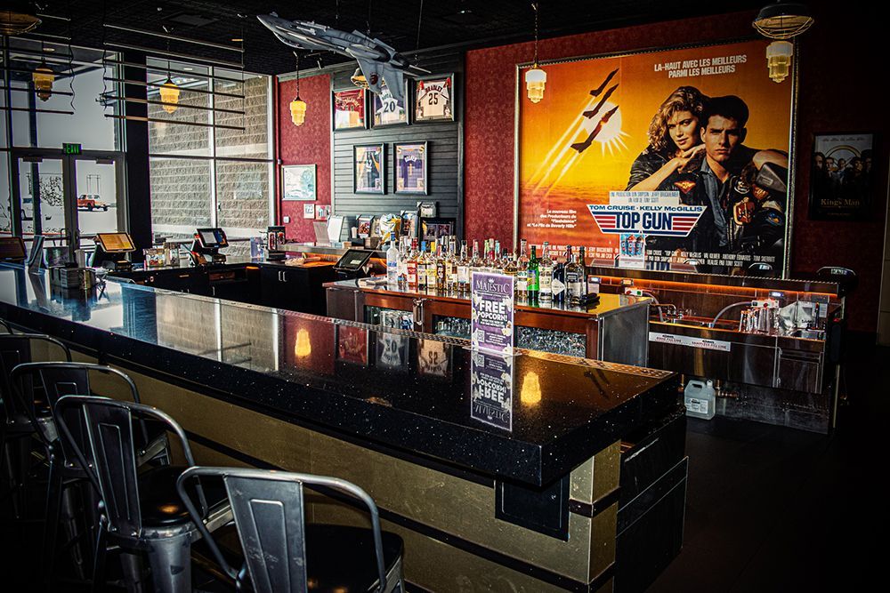 Bar with a Top Gun movie poster, drinks, and bar stools. Dark interior with a retro vibe.