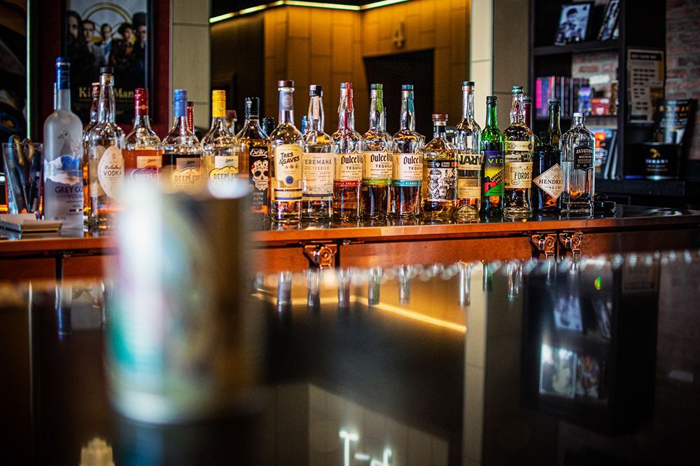 Bar with liquor bottles on display behind a polished counter, a cocktail shaker in the foreground.