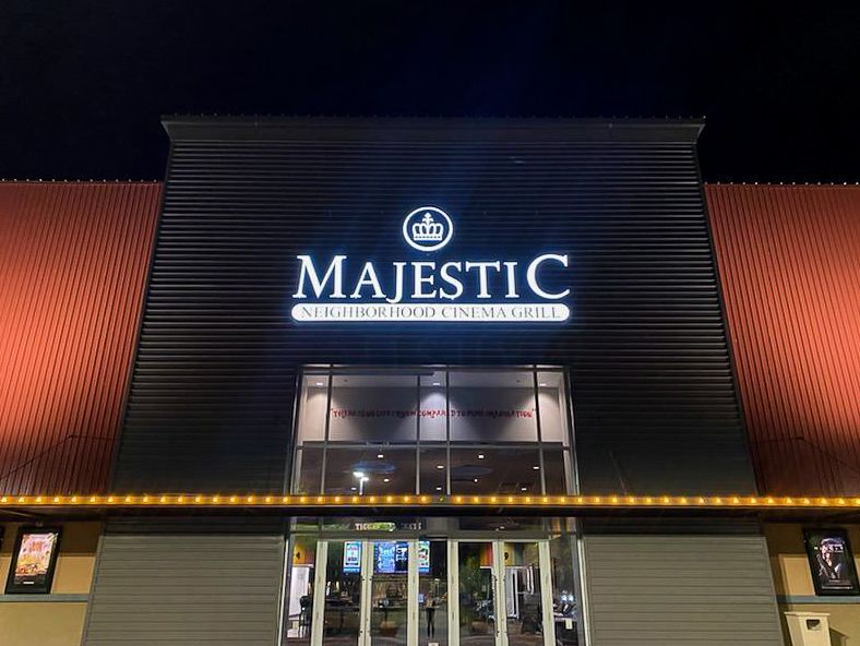 Majestic movie theater exterior, illuminated sign at night, entrance below, red roof, black facade.