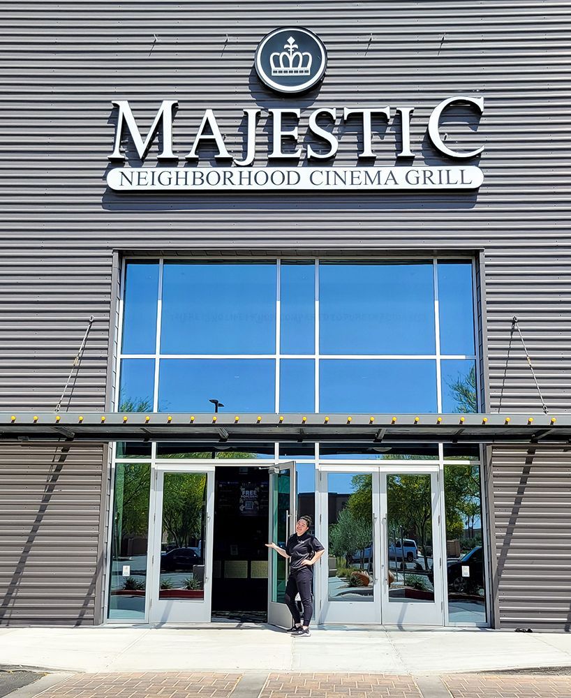 Majestic Neighborhood Cinema Grill exterior. Gray building with large windows and sign, person standing in doorway.