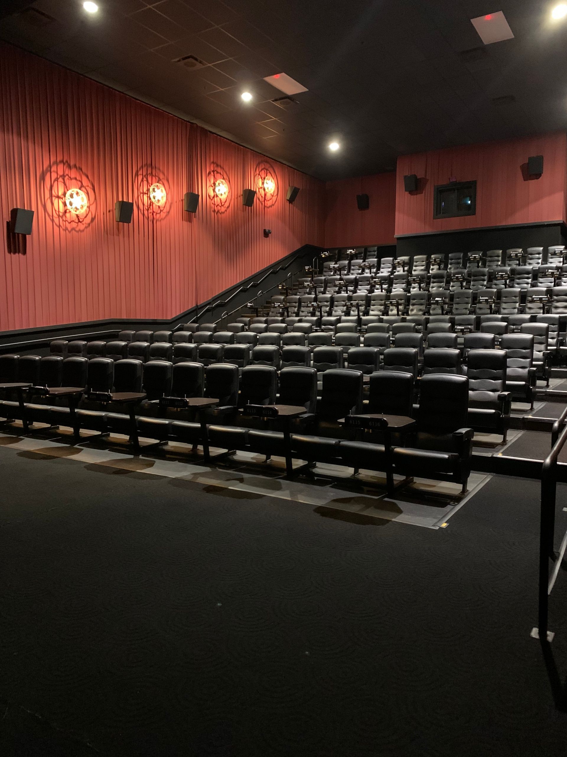 Empty movie theater with rows of black seats and red walls.