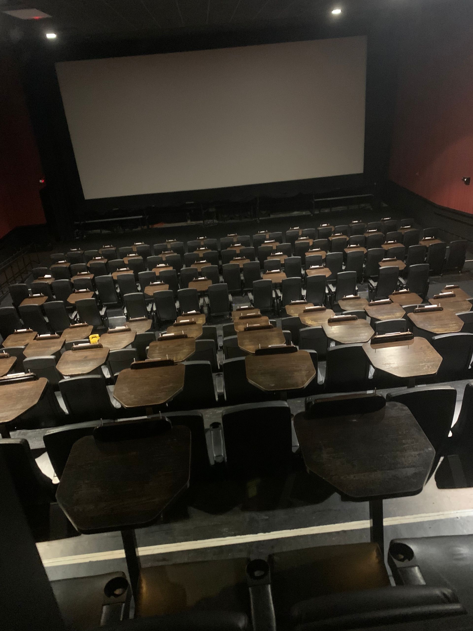 Empty movie theater with rows of black seats facing a large white screen.