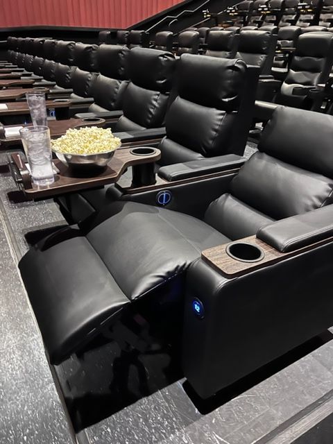 Rows of black leather reclining theater seats with side tables and food.