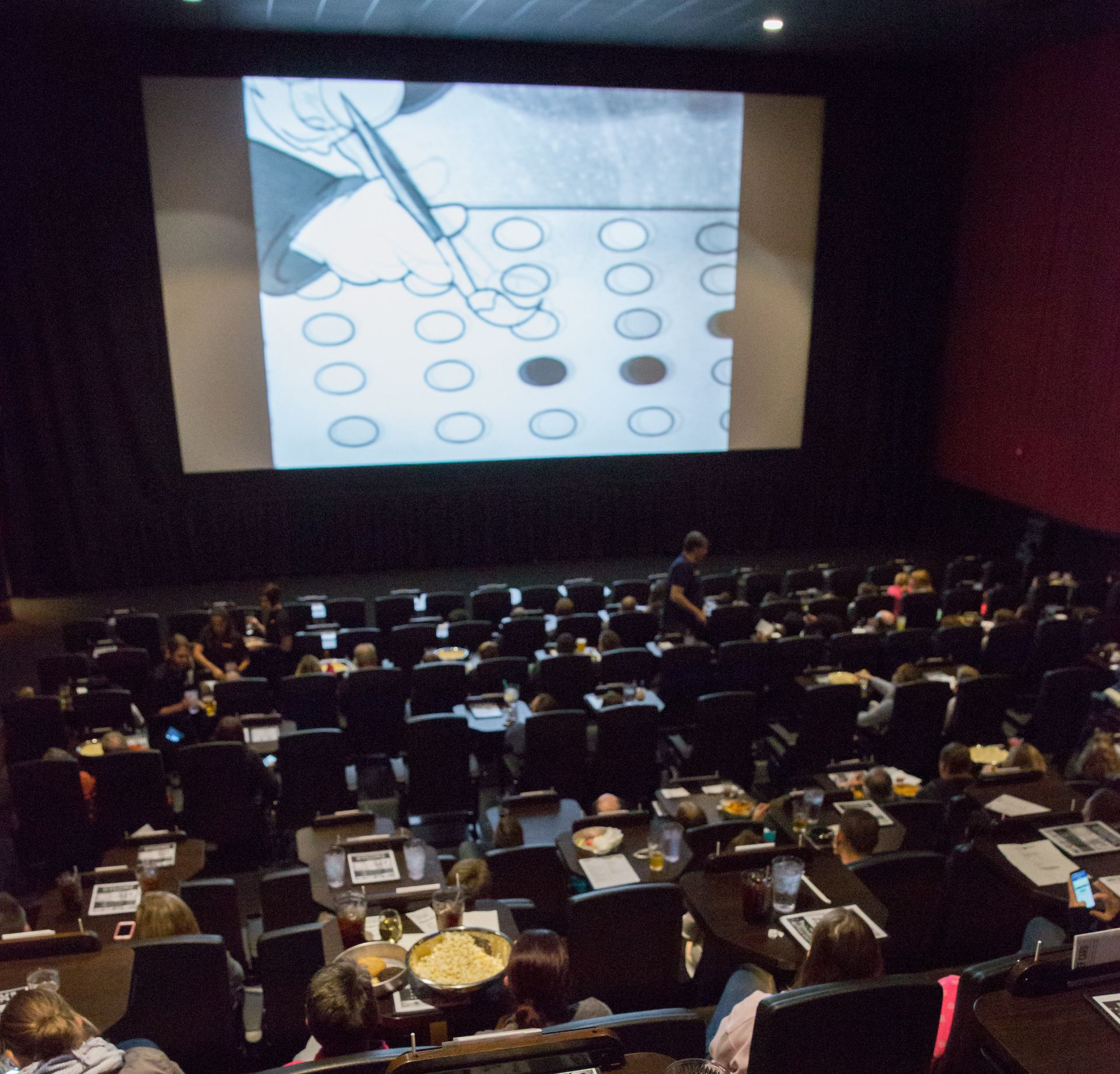 Audience watching a film in a theater. The movie screen shows a black and white animated graphic.