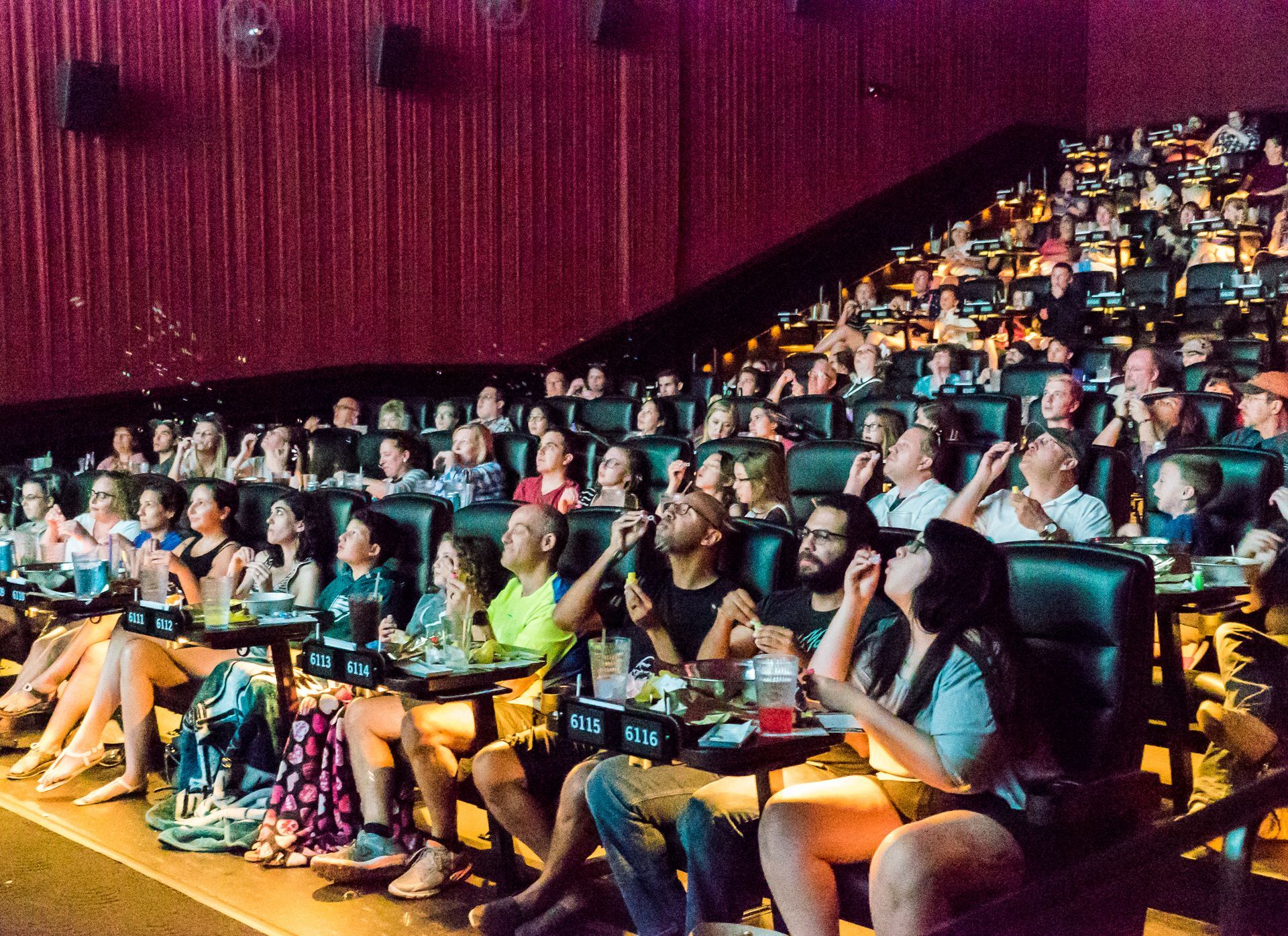 Audience in a movie theater watching a screen. People are looking up, some eating snacks.