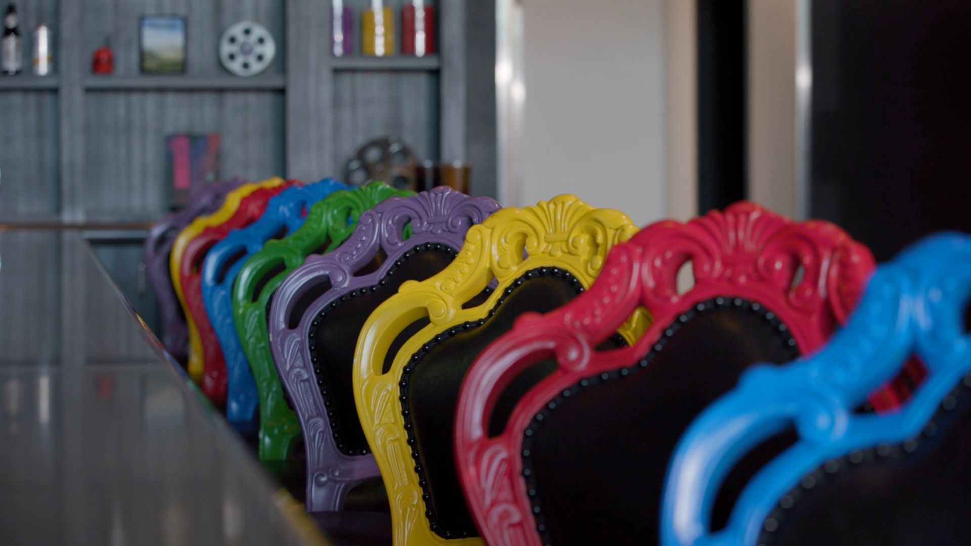 Row of colorful ornate chairs, red to blue, lined up against a counter.