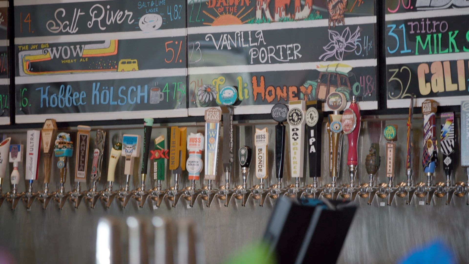 Rows of beer taps with chalkboard menu overhead, in a bar setting.