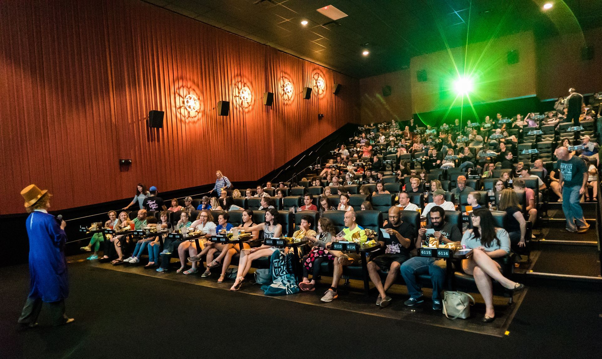 Audience watching a movie in a theater. People sitting, a person on stage, green light, dim lighting.