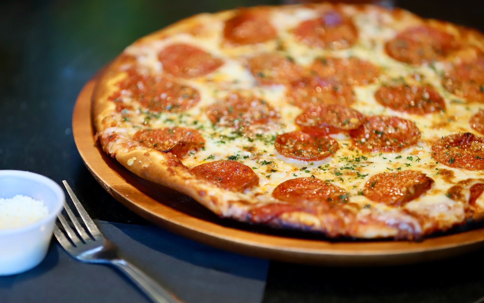 Pepperoni pizza on wooden plate with fork and small cup.