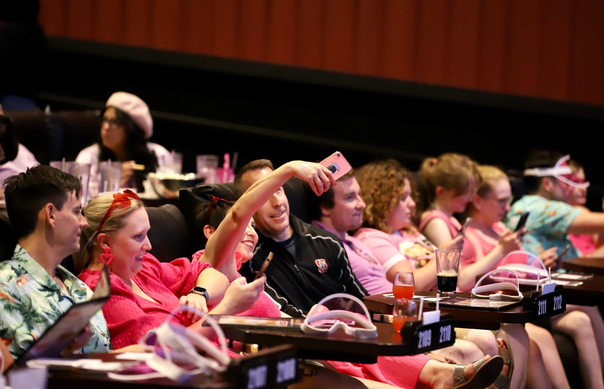 People in a movie theater, some wearing pink, taking selfies.