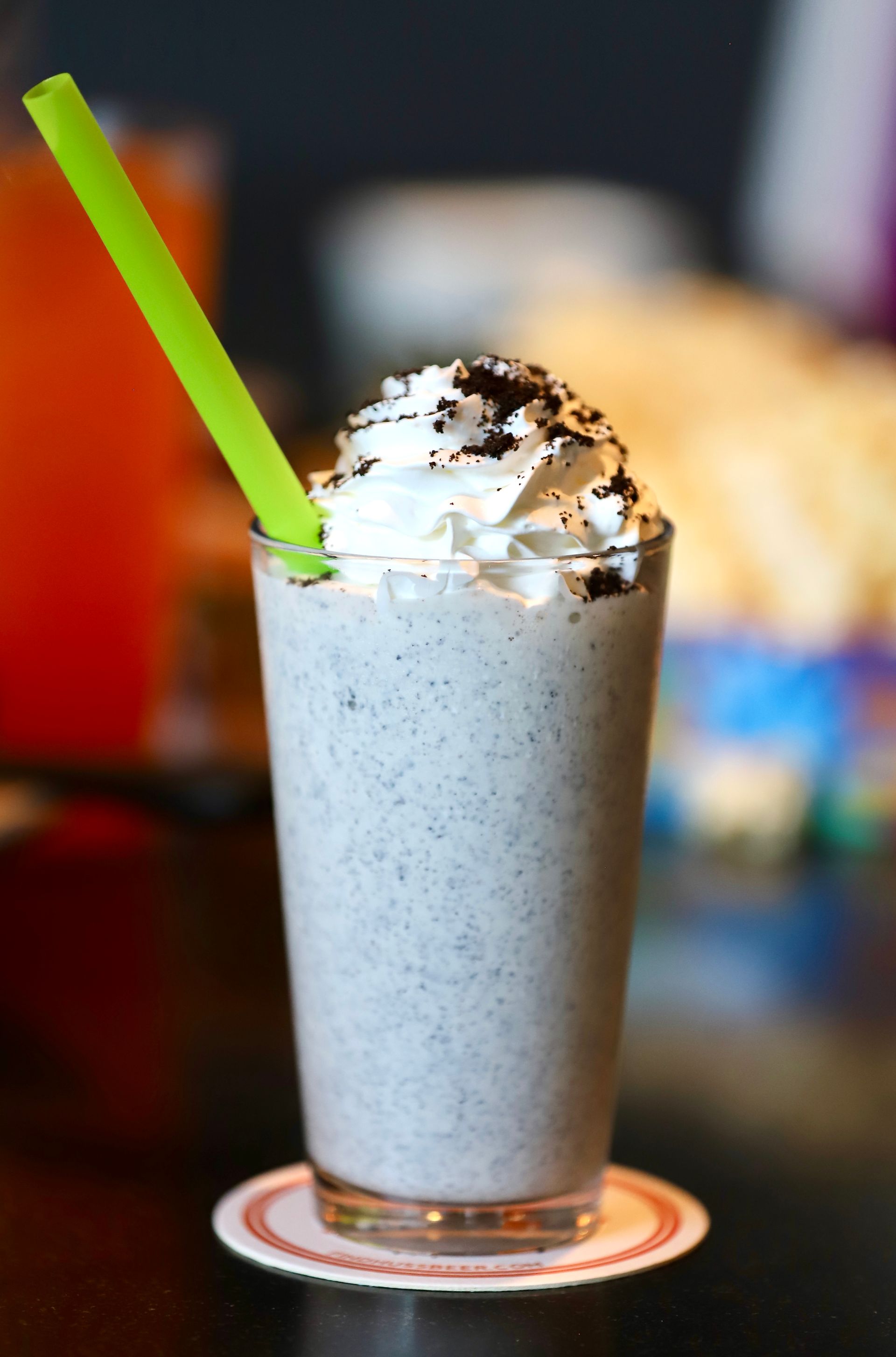 Cookies and cream milkshake in a glass, topped with whipped cream and cookie crumbs, green straw.