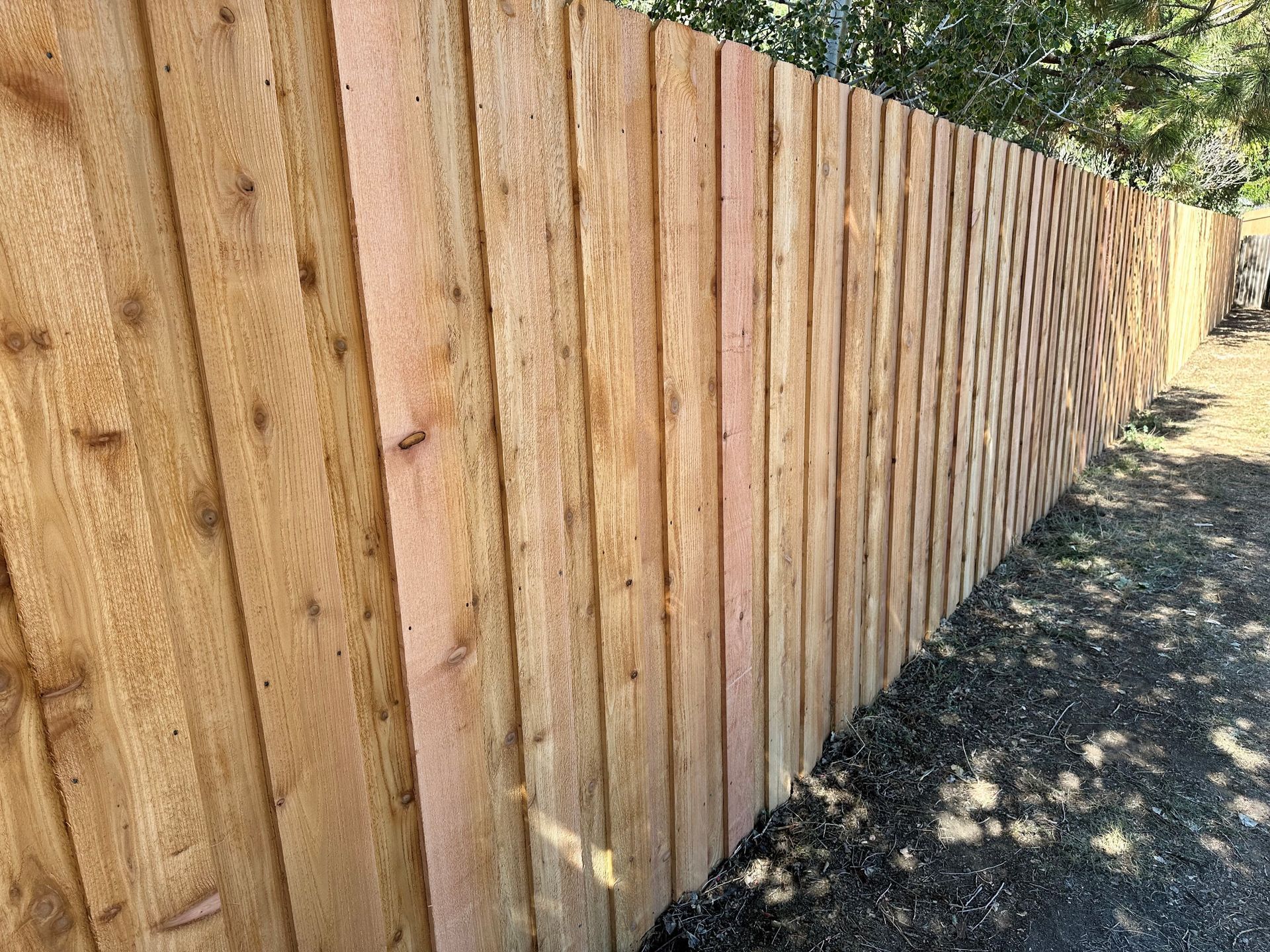 A wooden fence is sitting on the side of a dirt road.