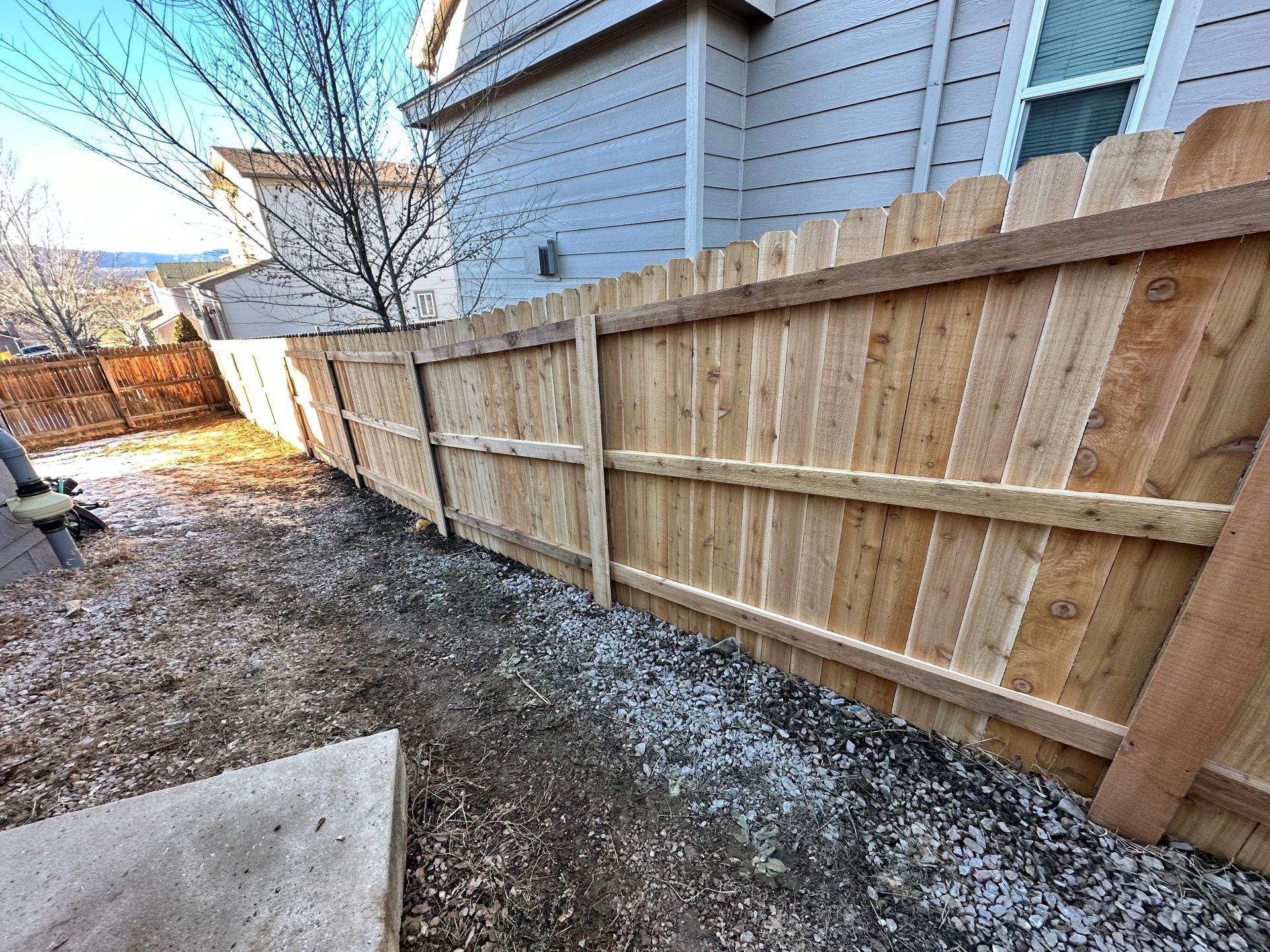 A wooden fence is in the backyard of a house.