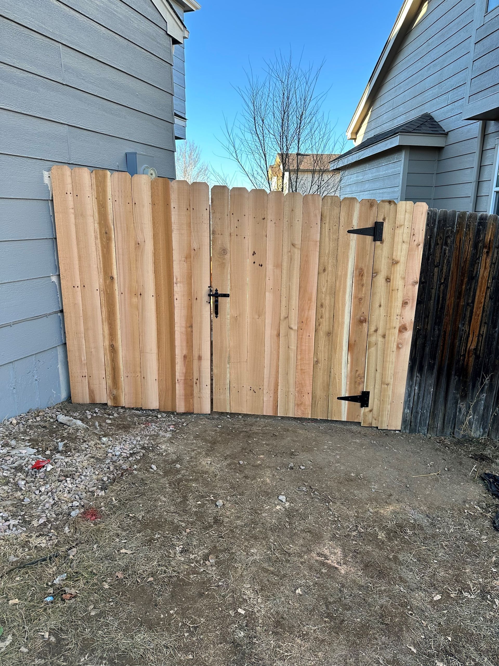 A wooden fence with a gate between two houses.