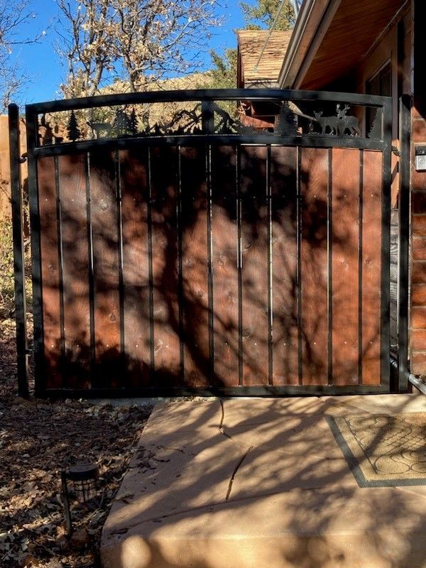 A wrought iron gate with a wooden fence in front of a house.