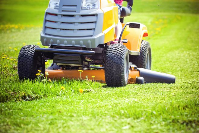A yellow riding lawn mower cuts grass in a bright, green field.