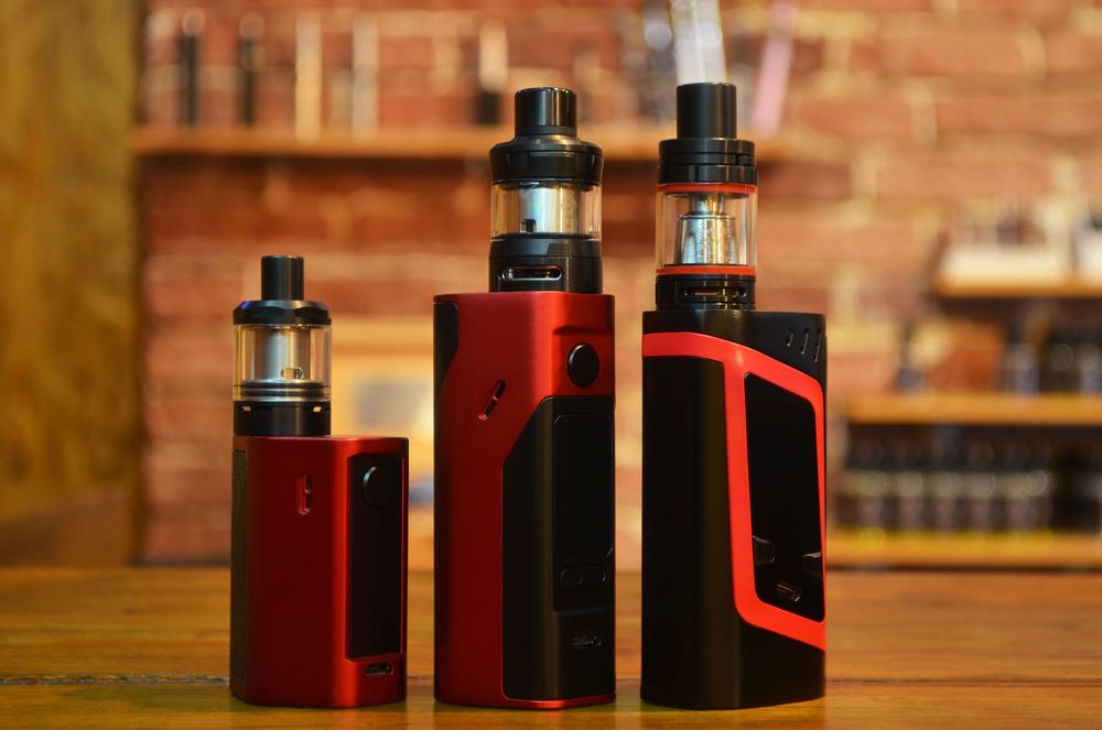 Three electronic cigarettes are sitting on a wooden table.