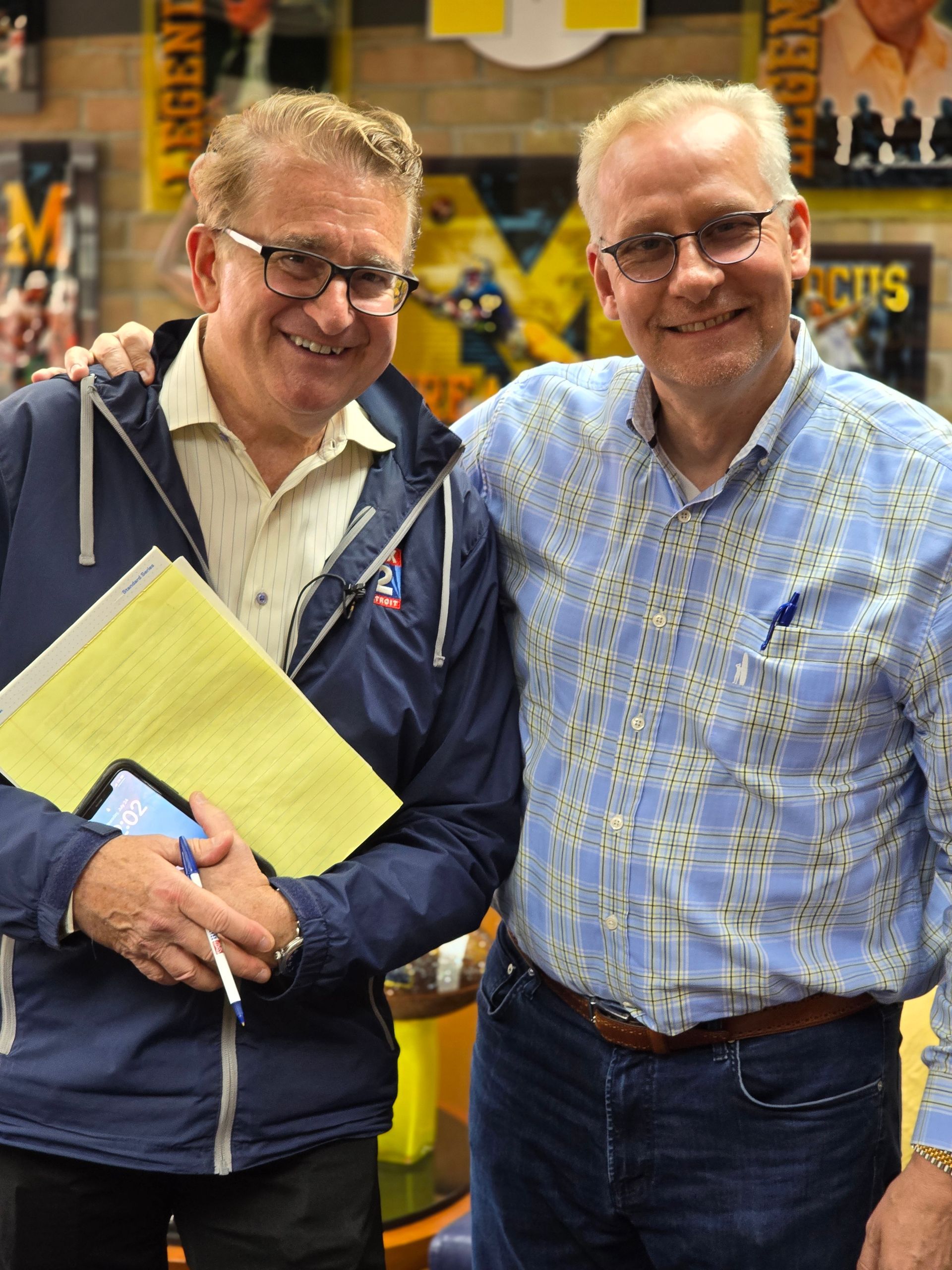 Two men are posing for a picture and one of them is holding a piece of paper.