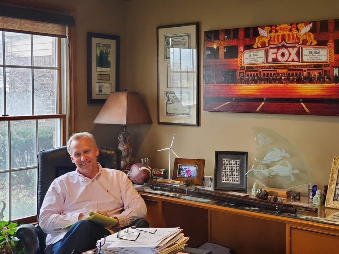 A man is sitting in a chair in front of a fox sign on the wall.