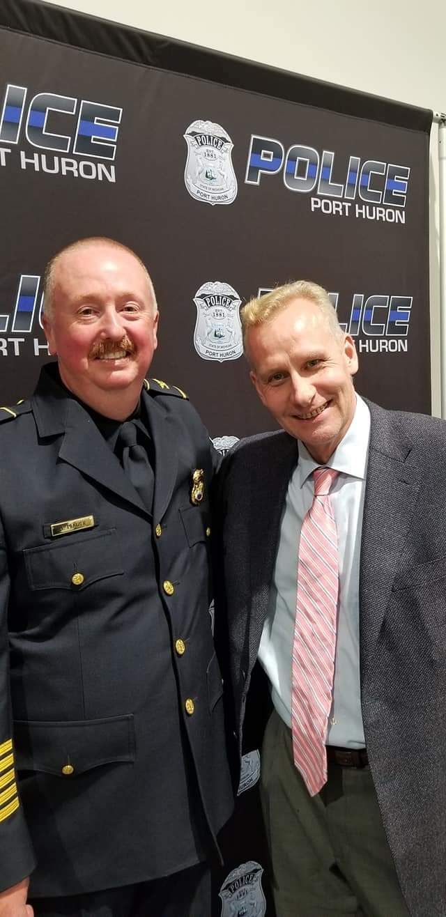 Two men are posing for a picture in front of a police sign.