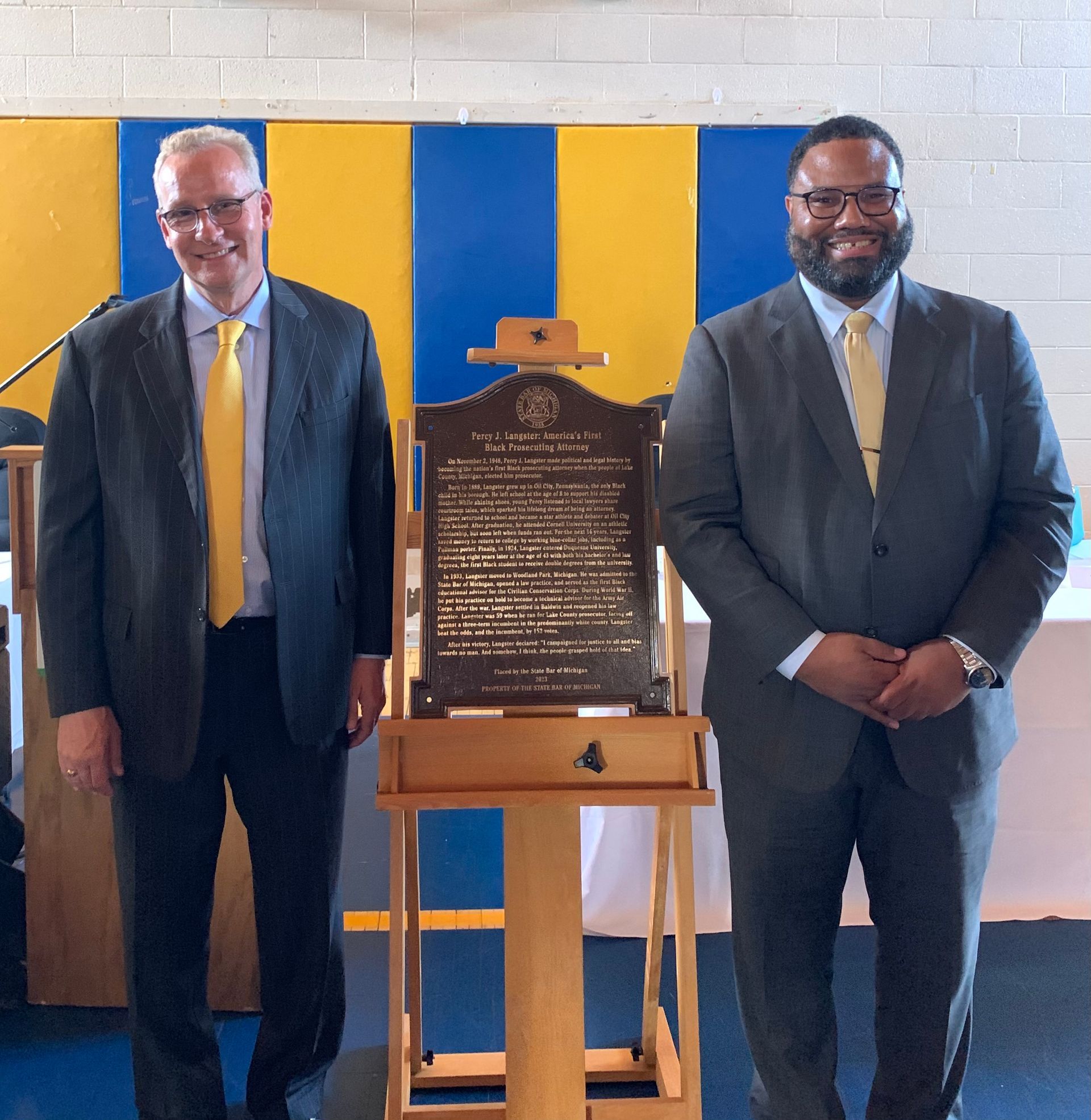 Two men in suits and ties standing next to a plaque