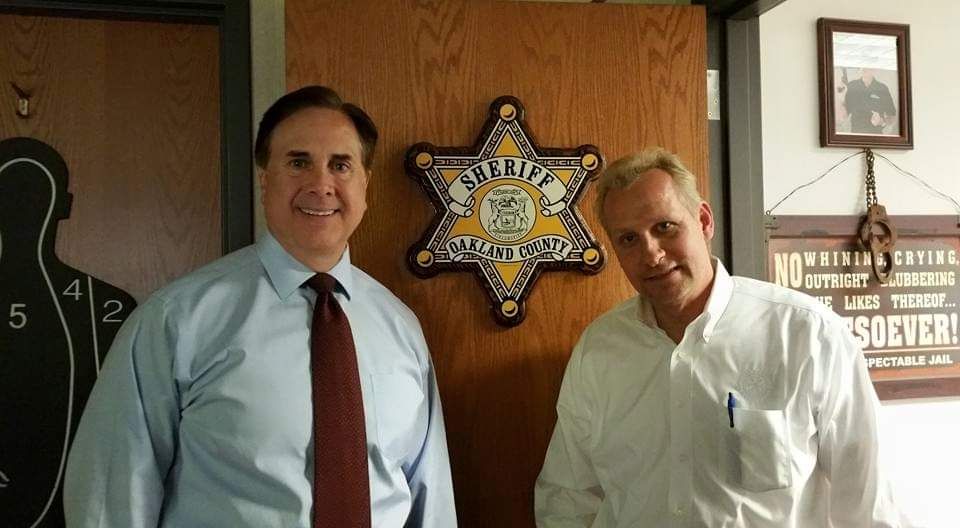 Two men shaking hands in front of a sheriff 's badge
