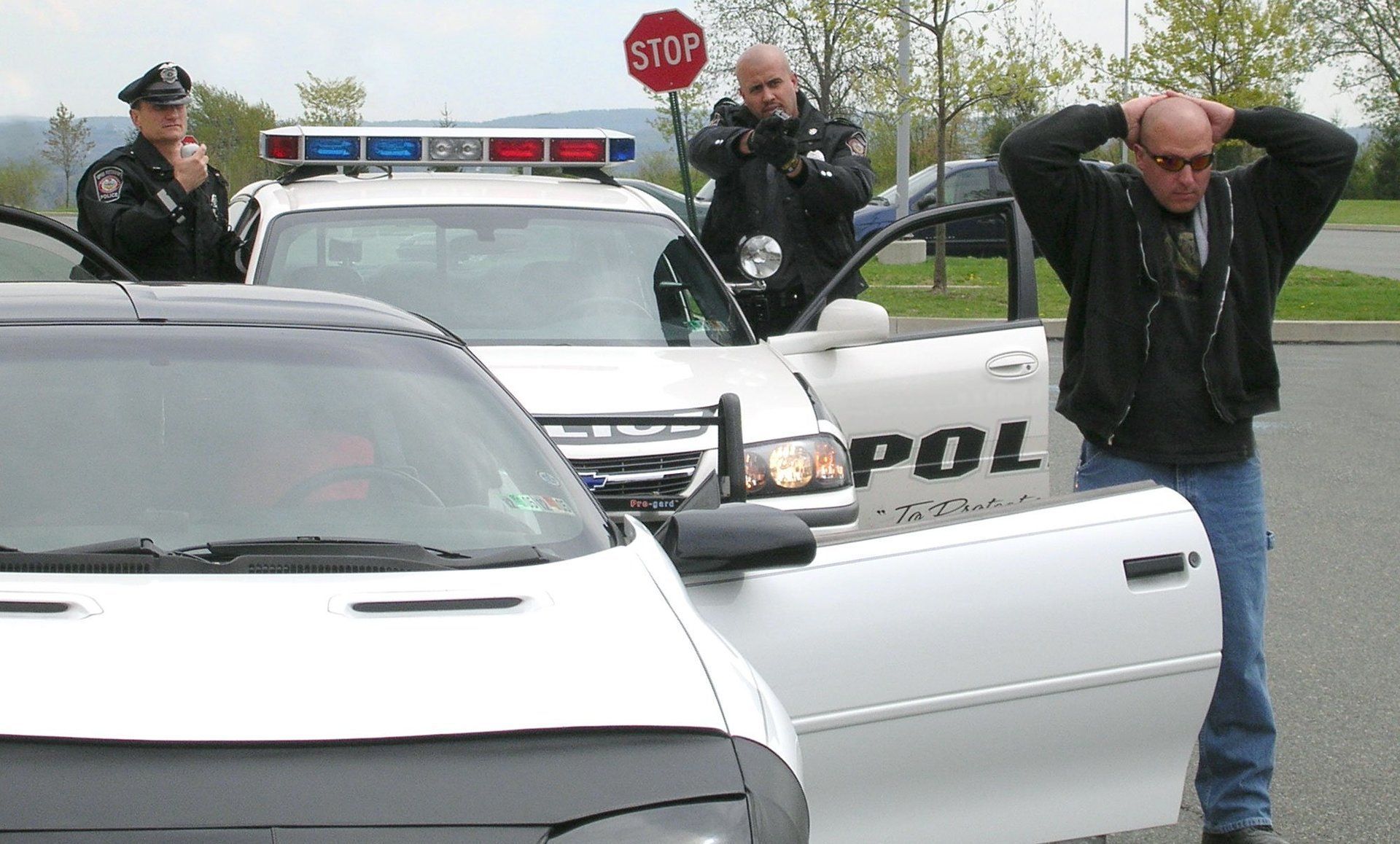 A man is standing in front of a white police car