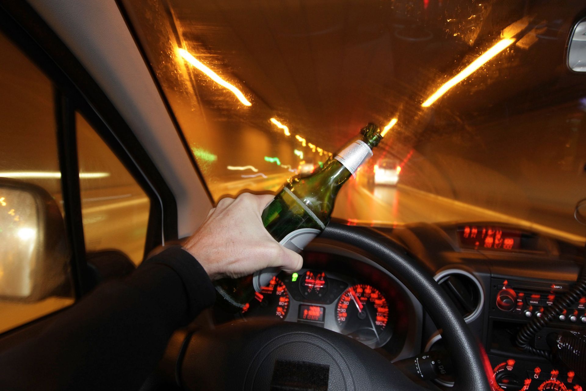 A person is driving a car with a bottle of beer in their hand.