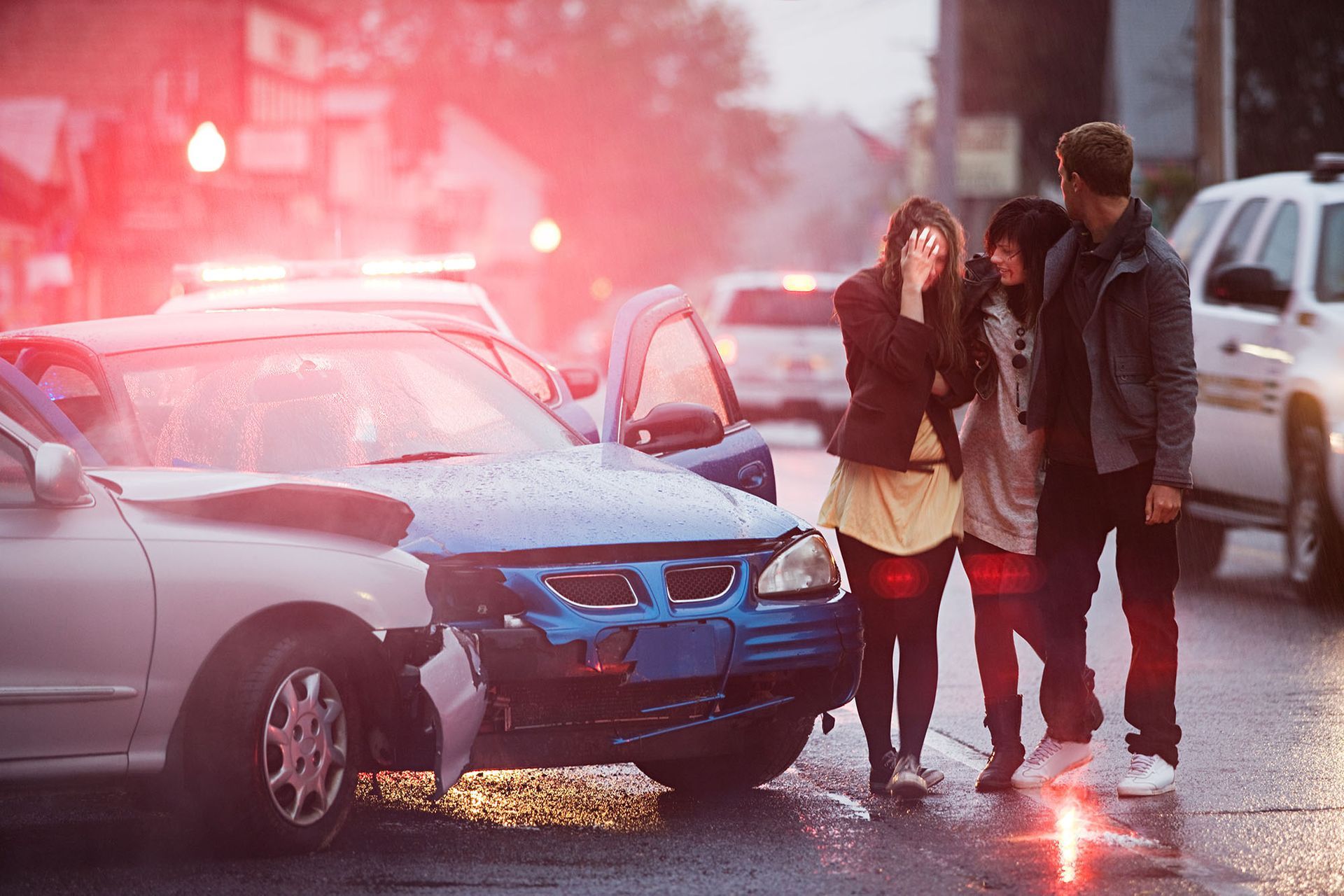 A group of people are standing next to a car that has been involved in a car accident.