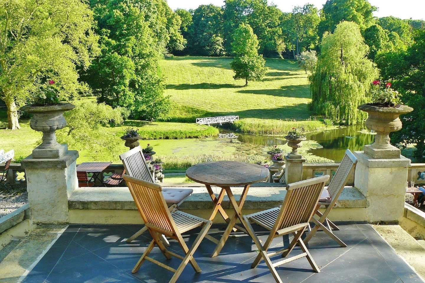 Patio table and chairs overlooking a lush green garden and pond on a sunny day